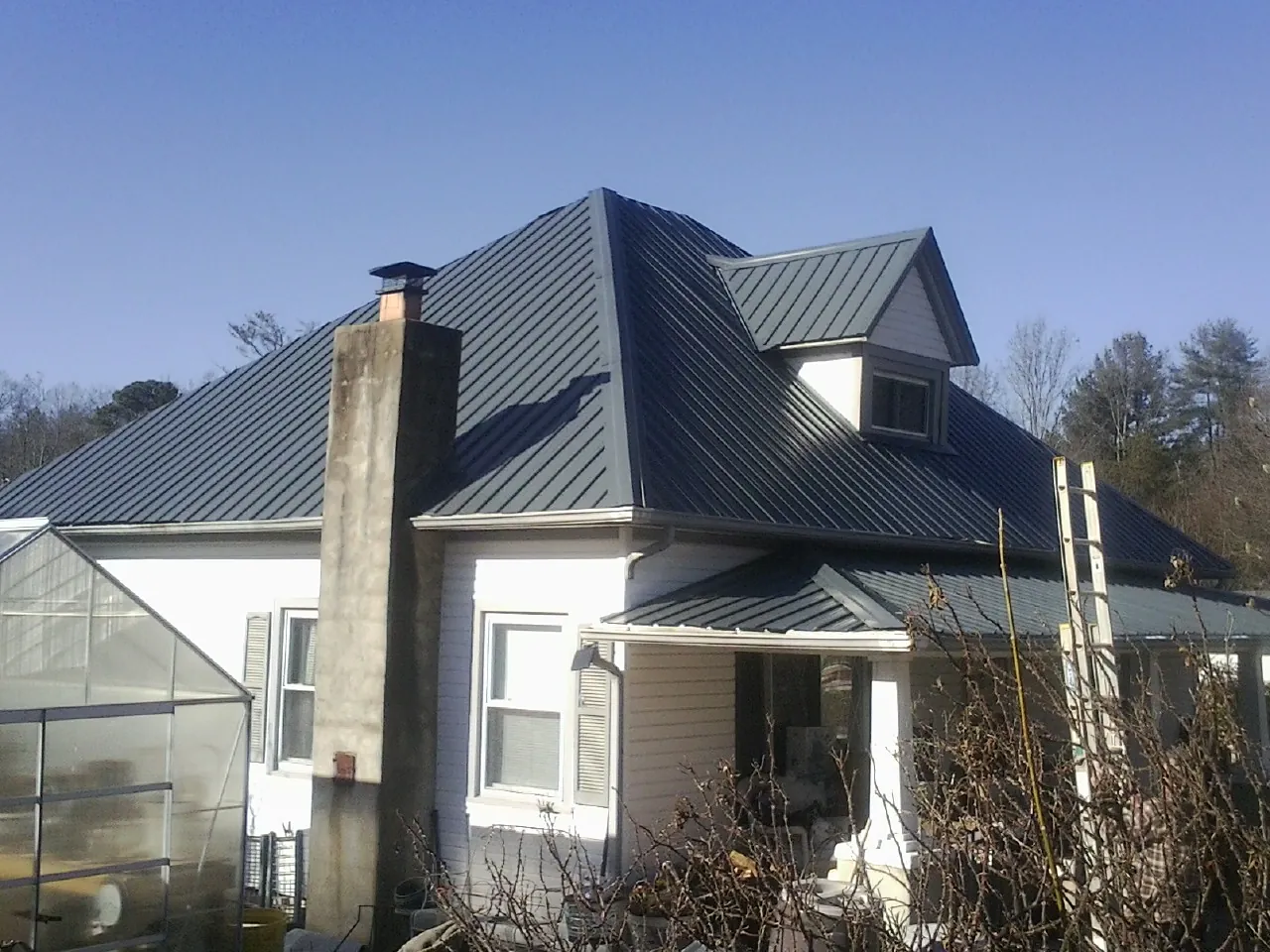 Dark blue standing seam metal roof on a white farmhouse with dormer — Slate & Tile Roof Repair by Roofing Brothers in Maidsville