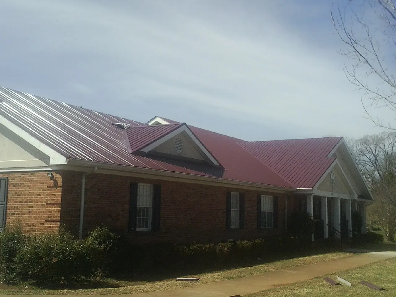 Red metal roof with gabled entries on a long brick building, from a Hail Damage Roof Repair job in Maidsville