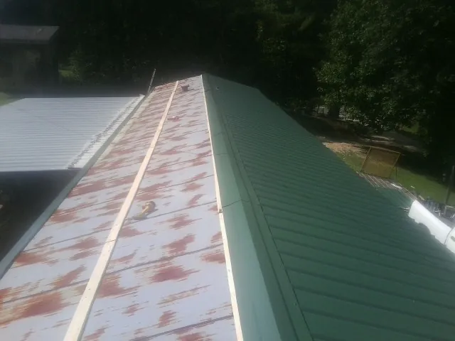 Old rusted panels beside newly installed green metal roofing — Wind Damage Roof Repair by Roofing Brothers in Maidsville