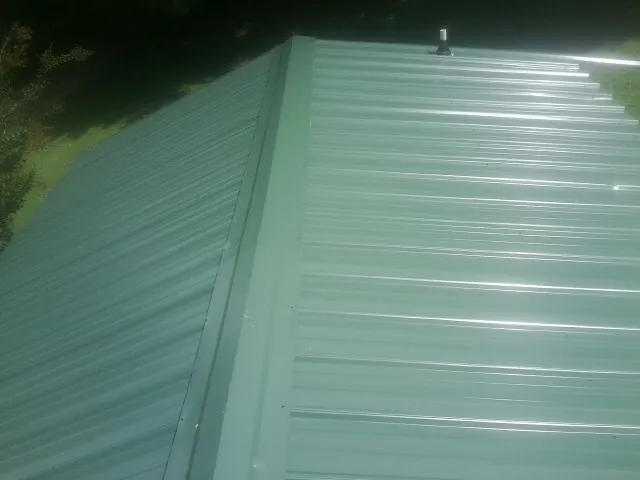 New green metal panels meeting at the ridge of a roof — Flat Roof Repair work by our crew in Maidsville