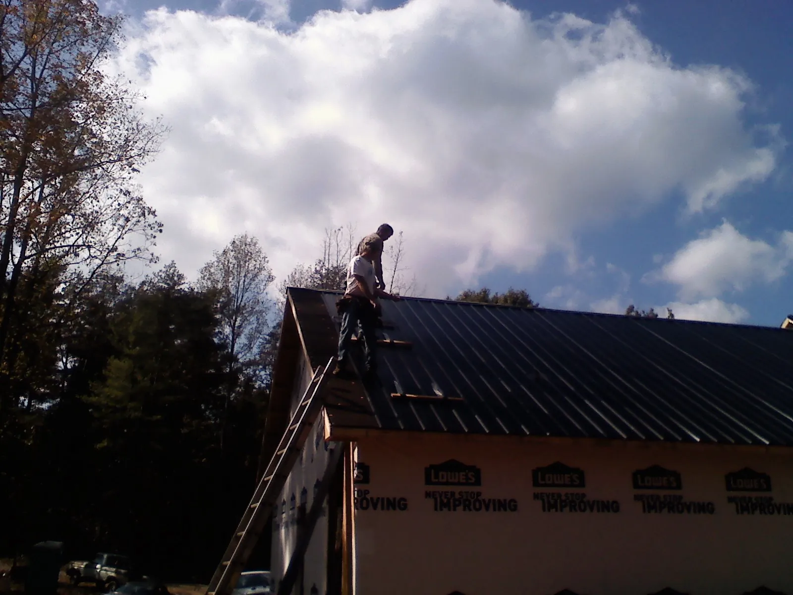 Roofer fastening dark metal panels high against a cloudy sky, from a Roof Inspection job in Maidsville