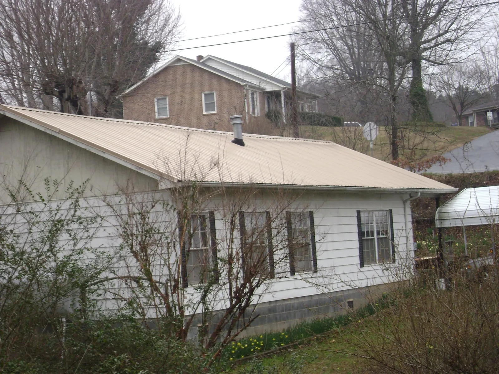 Tan metal roof on a white sided house set into a hillside — Commercial Roofing by Roofing Brothers in Maidsville